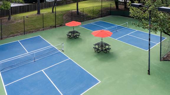 A tennis court with two red umbrellas and two benches.