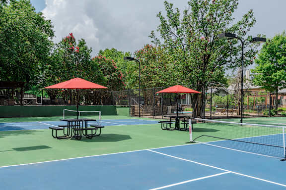 A blue tennis court with red umbrellas and benches.