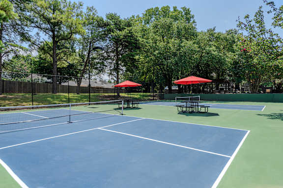 A tennis court with a net and two red umbrellas.