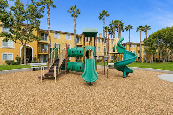 A playground with a green slide and a brown sandy ground.