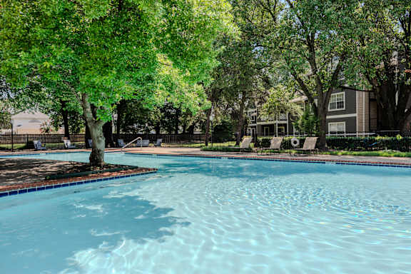 A swimming pool surrounded by trees and a building in the background.