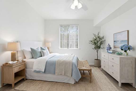 A bedroom with a bed, nightstand, and a plant.