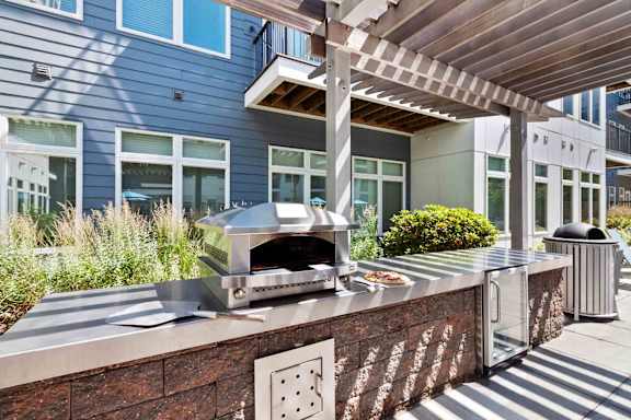 A modern outdoor kitchen with a pizza oven and a trash can.