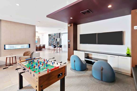 A foosball table is in the middle of a room with a TV and bean bag chairs.