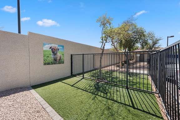 A black metal fence surrounds a grassy area with a poster of a dog on the wall.