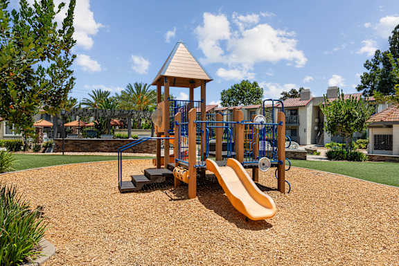 A playground with a yellow slide and a wooden structure.