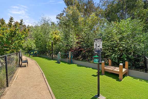 A fenced dog park with agility equipment and a bench.