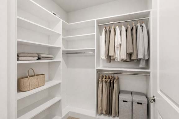 A white closet with clothes hanging and baskets on the shelves.