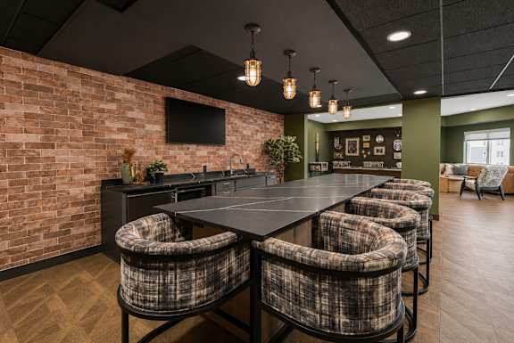 A room with a long table and chairs with a brick wall on one side.