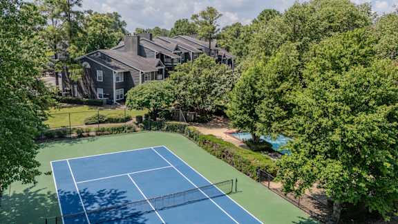 A tennis court surrounded by trees and a building in the background.