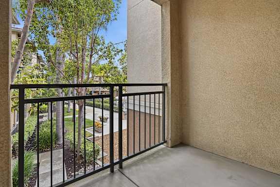 A balcony with a black railing and a view of a tree and a building.