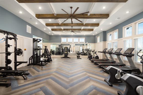 a gym with cardio machines and windows and a ceiling fan
