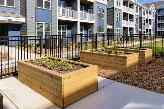 Apartment complex with a black fence and two wooden planters with green plants in front.
