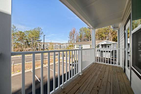 A white railing on a wooden deck overlooks a parking lot and buildings.