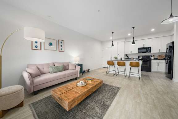 A modern living room with a pink couch, a wooden coffee table, and a kitchen area in the background.