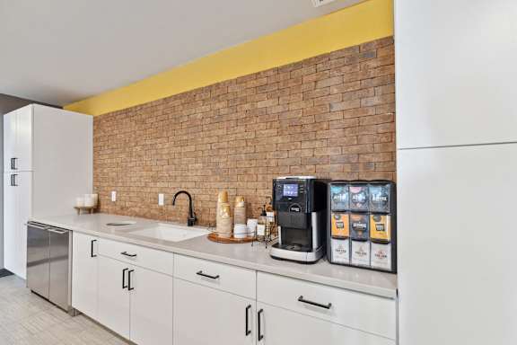 A kitchen with a brick wall and white cabinets.