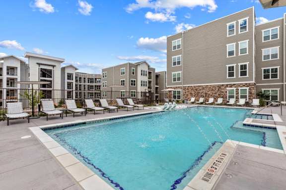 A large swimming pool surrounded by lounge chairs and buildings.
