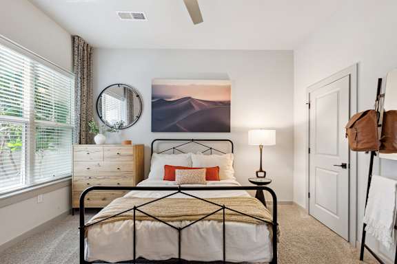 A bedroom with a bed, a lamp, a mirror, and a painting on the wall.