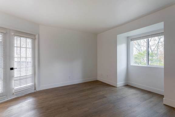 A room with white walls and wooden flooring with a window on the right.