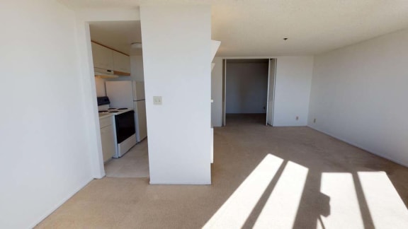 an empty living room with a kitchen in the background