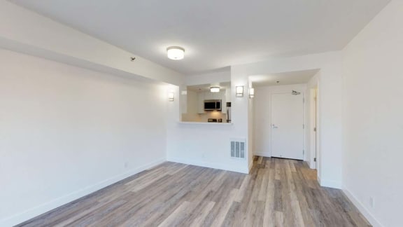 an empty living room with a kitchen in the background
