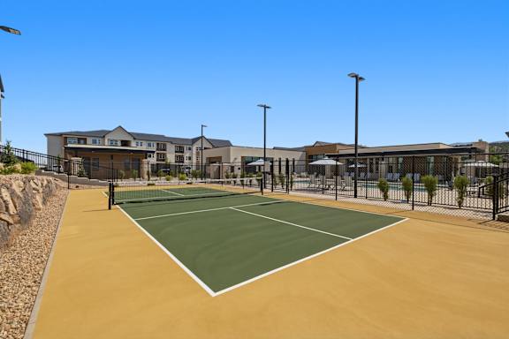 A tennis court is surrounded by a fence and a building.