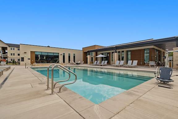 A swimming pool with a metal ladder and lounge chairs.