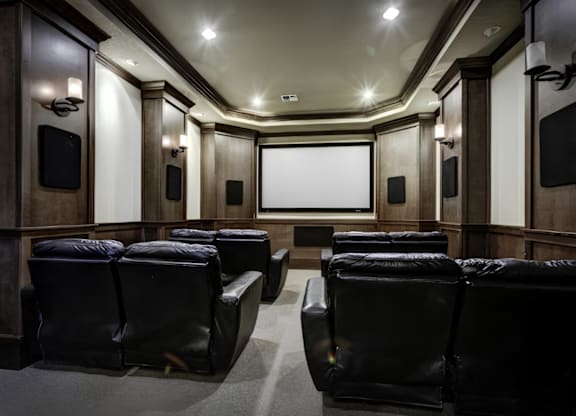 A dark cinema room with black leather seats and a screen at the front.