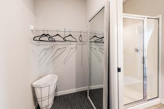 a closet with a mirror and a trash can in a bathroom with a glass shower