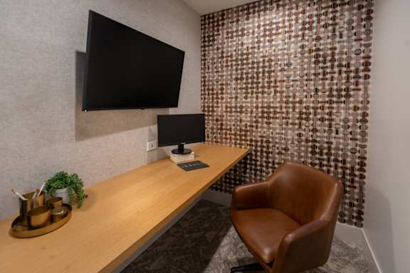 A brown leather chair sits in front of a desk with a black monitor and a lamp.
