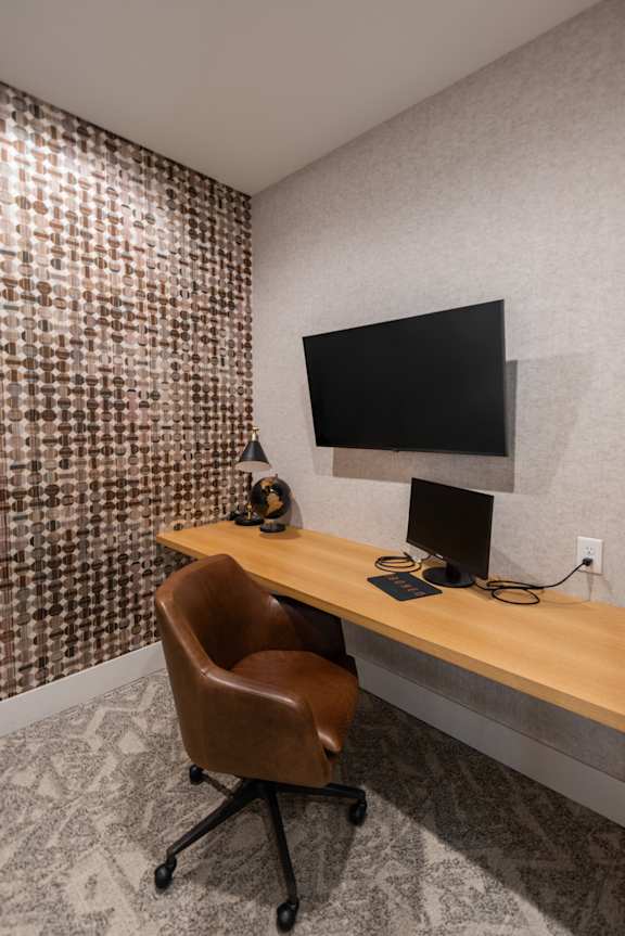 A brown leather chair sits in front of a wooden desk with a flat screen TV mounted on the wall.