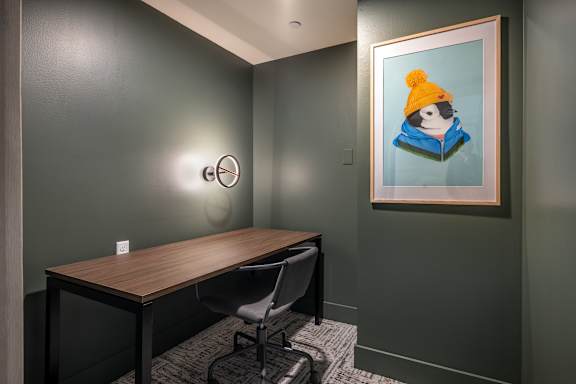 A painting of a penguin wearing a yellow hat is hanging on a wall above a desk.