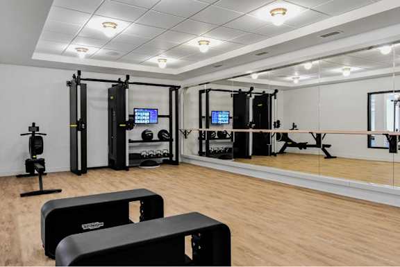 A gym with a variety of equipment including a treadmill, a stationary bike, a rowing machine, a squat rack, a bench press, a cable machine, and a mirror.