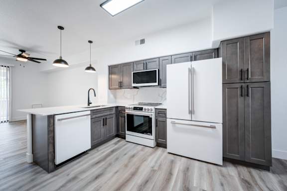 A modern kitchen with a white refrigerator, white countertops, and dark wood flooring.