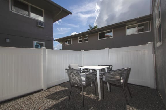 an oversized patio with a table and chairs in front of a white fence at Mala Grove in Hawaii,  96797