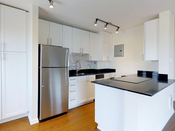 A kitchen with white cabinets and a black countertop at Skye at Belltown Apartments, Seattle, WA 98121