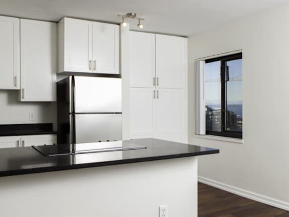 A kitchen with white cabinets and a black countertop at Skye at Belltown Apartments, Seattle, WA