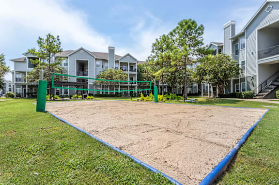 A sand volleyball court is surrounded by apartment buildings.