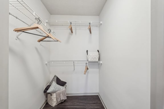 A white closet with clothes hanging and a basket on the floor.