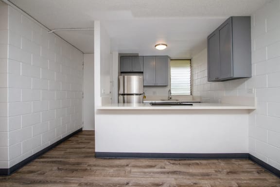 View from the living room with plank flooring into the kitchen with grey shaker-style cabinets at Palms of Kilani in Wahiawa, Hawaii
