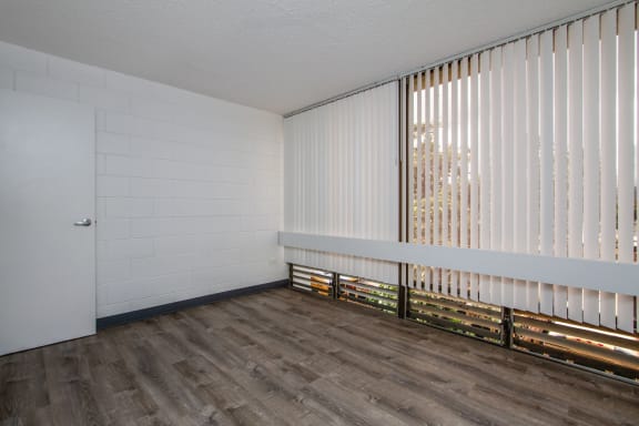 an empty living room with white vertical blinds on the oversized windows at Palms of Kilani in Wahiawa, Hawaii