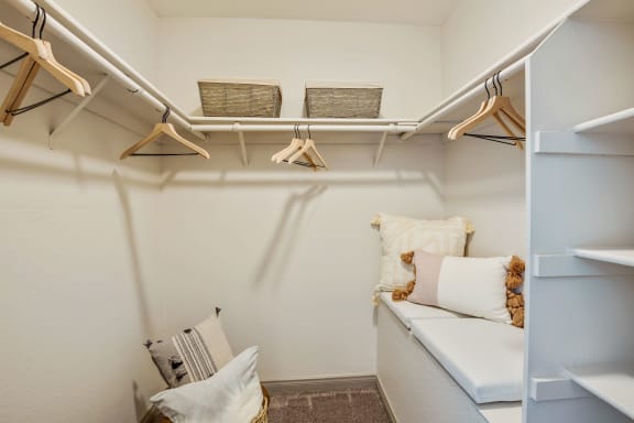 a walk in closet with white shelves and pillows