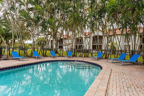 A pool surrounded by trees and chairs.