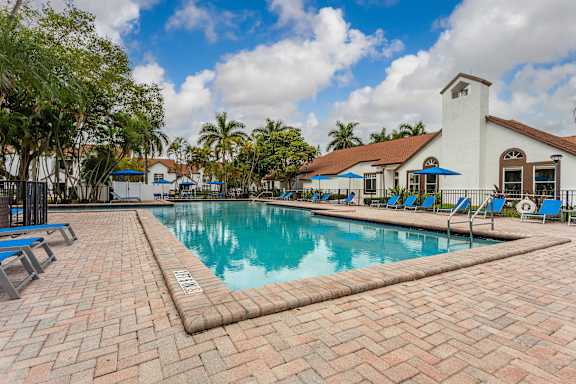 A pool with a brick walkway and a white building in the background.