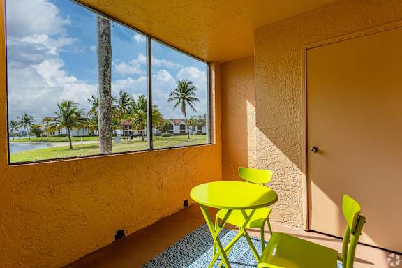 A yellow table and chairs are in front of a window with a view of a palm tree and a blue sky.