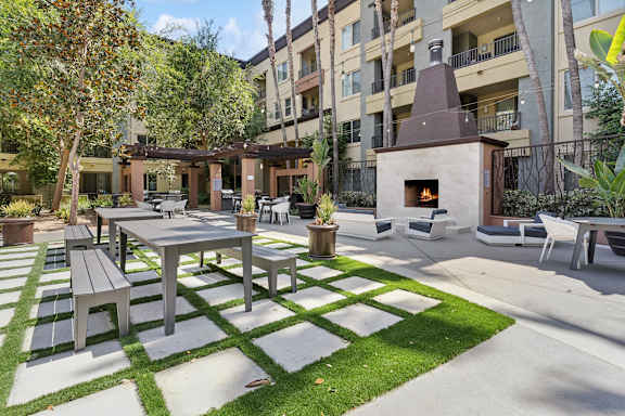 A patio with a table and chairs is surrounded by a grassy area and apartment buildings at The Kitt at Warner Center Apartments, Woodland Hills