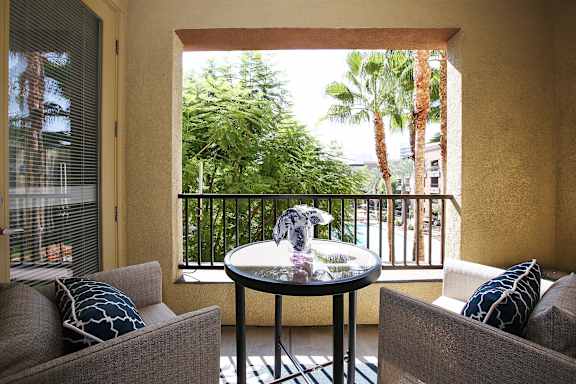 A balcony with a table and two chairs overlooking a lush green area. at The Kitt at Warner Center Apartments, California, 91303