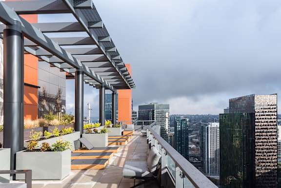 A long walkway with a roof and planters on either side leading to a cityscape.