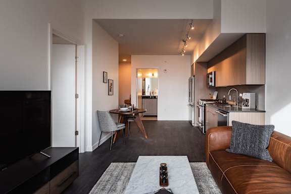 A modern living room with a brown leather couch and a grey rug.
