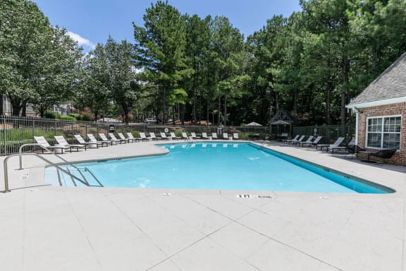 a swimming pool with chairs around it and trees in the background at Gwinnett Pointe, Norcross
